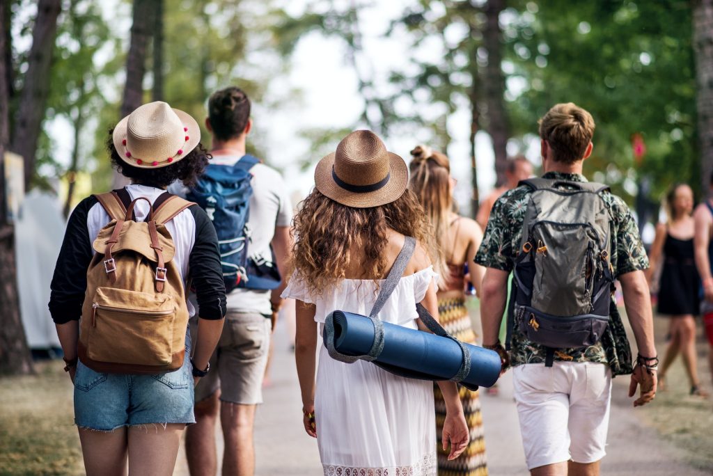 Rear view of group of young friends with backpack walking at summer festival.